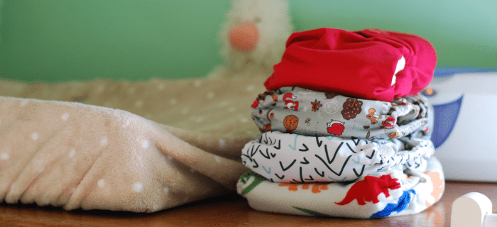 A pile of reusable nappies in multiple colours and patterns. The pile of nappies are to the right of a changing mat.