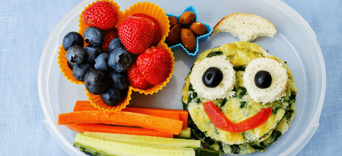 A lunch box with strawberries, blueberries, carrot sticks and a healthy snack with a face on it