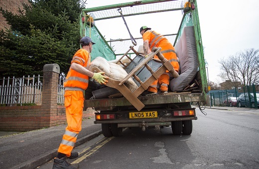 Two men in high vis loading an old sofa into a caged vehicle