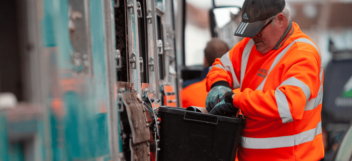 A Bristol Waste recycling collector takes items from a black box and puts them into the side of the truck