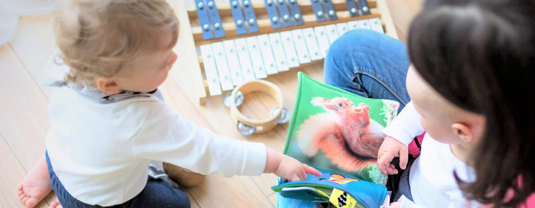 An adult playing with two young children surrounded by wooden toys