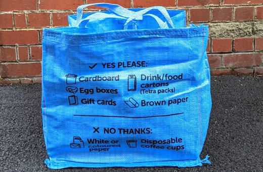 A Bristol Waste blue bag for card and brown paper in front of a red brick wall.