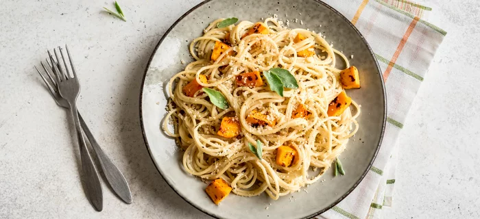 A plate of spaghetti with pumpkin chunks
