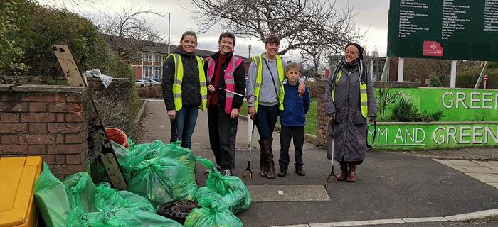 A group of five people standing behind their bags of litter that they collected
