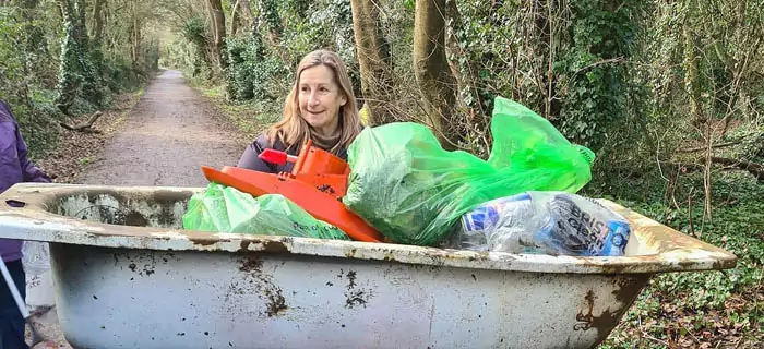 A litter picker push a shopping trolley full of litter, including a bath tub.