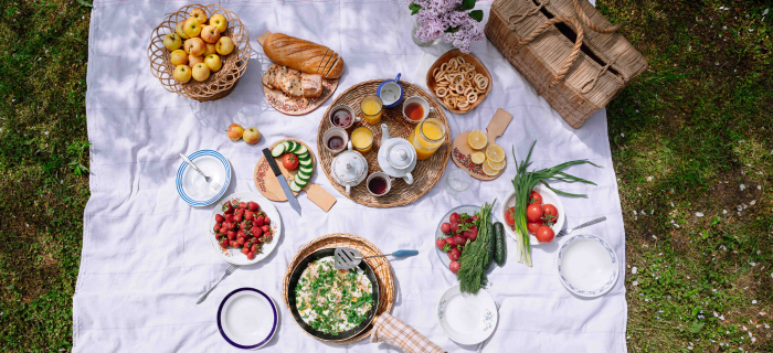 A plastic-free picnic spread on top of a white sheet on a grassy lawn.