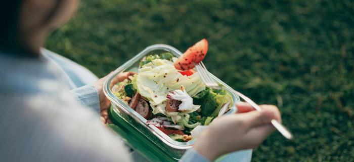 A woman uses reusable cutlery to eat a packed lunch out of a tupperware box. 