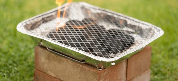 A disposable BBQ raised off the grass with bricks.