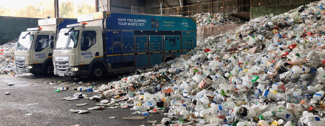 Two Bristol Waste recycling trucks inside the plastic bay at the transfer station. A mountain of plastic recycling fills half the frame.