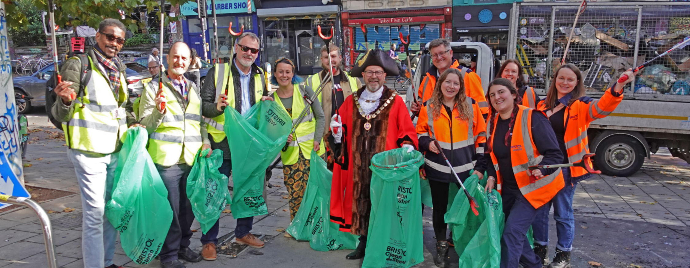 A group of people in hi-vis pose with bags of litter and litter picking sticks. They are all smiling