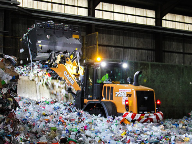 A tractor is scooping plastic recycling up onto a conveyer belt to be recycled at the transfer station
