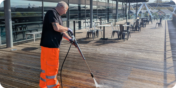 Man in hi-visibility trousers using a pressure washer on a deck