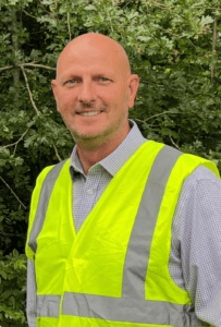 Rob Heath in a hi-vis vest, outdoors in front of trees