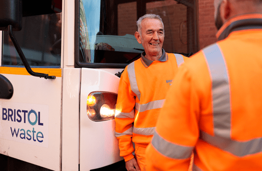 Two men in hi-vis smile whilst standing in front of a large truck
