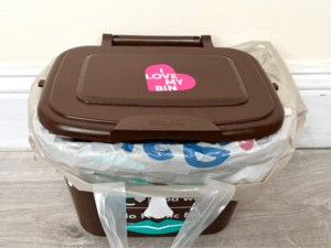 A brown Bristol Waste food recycling caddy sits on a counter top. It's been lined with a Tesco carrier bag