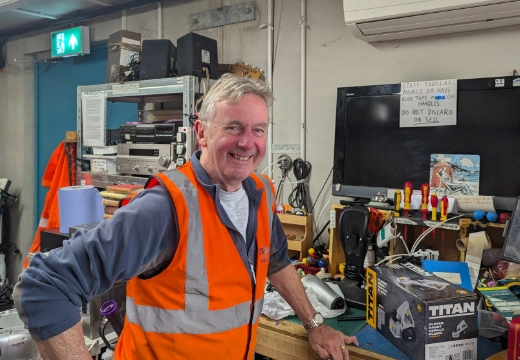 Man smiling standing next to a worktop with many tools behind him