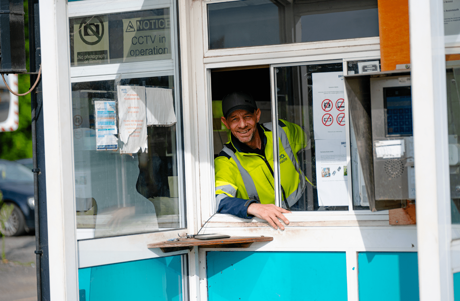 A smiling person leans out of the window in a porta cabin at the Bristol Waste transfer station