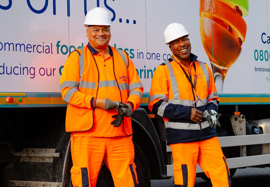 two men wearing hi-visibility clothing and safety helmets in front of a waste management truck