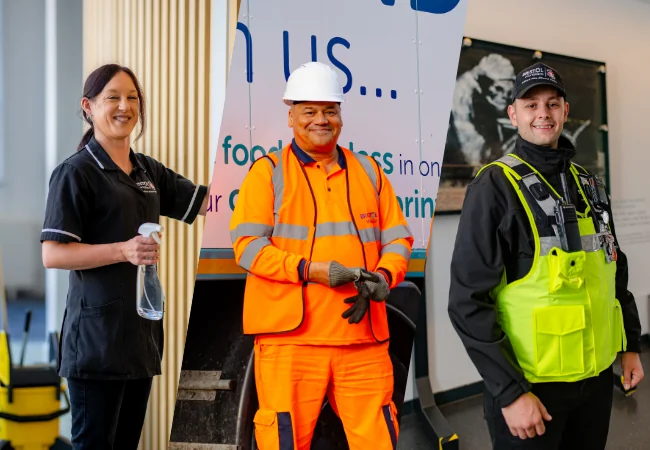 A woman cleaning, a man in high vis and hard hat, a man in security guard clothing