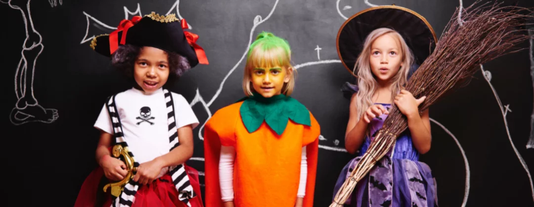 Three children dressed in halloween costumes: a pirate, a pumpkin and a witch.