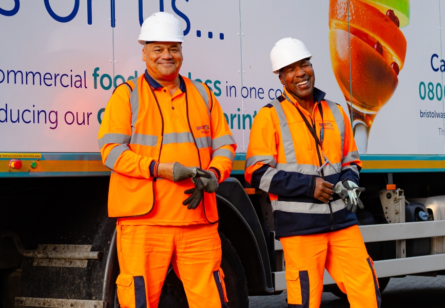 two men wearing hi-visibility clothing and safety helmets in front of a waste management truck