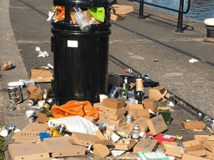 A bin on Bristol's harbourside is overflowing with rubbish. A mountain of old card and litter is on the floor next to it