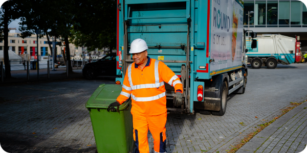 Man in hi-visibility clothing moving wheelie bin from a recycling truck