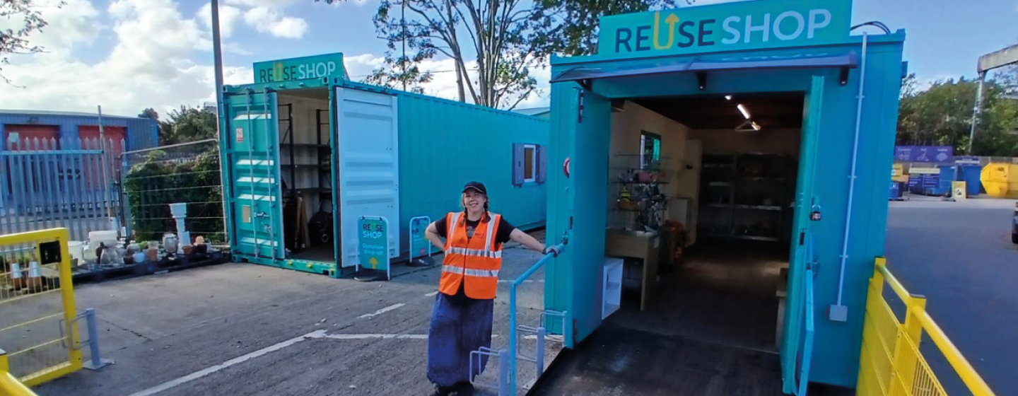 A woman in a hi-vis vest leans on a handrail outside of the Reuse Shop