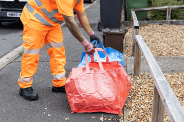 A man wearing hi-vis picks up recycling containers