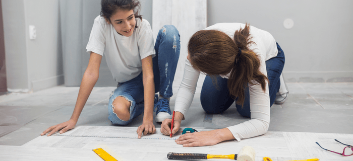 Two women kneeling to mark measurements on laminate flooring
