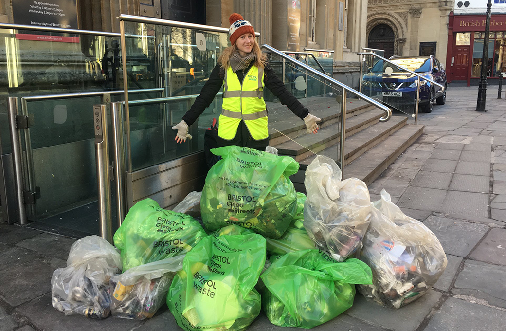 A woman stands behind a pile of litter bags with her arms outstretched