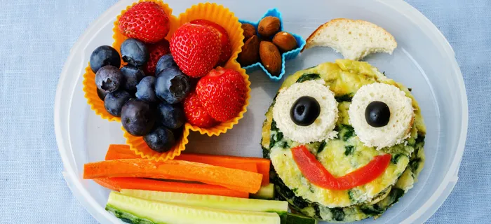 A lunch box with strawberries, blueberries, carrot sticks and a healthy snack with a face on it