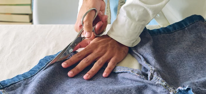 A pair of hands can be seen cutting the ends off a pair of jeans