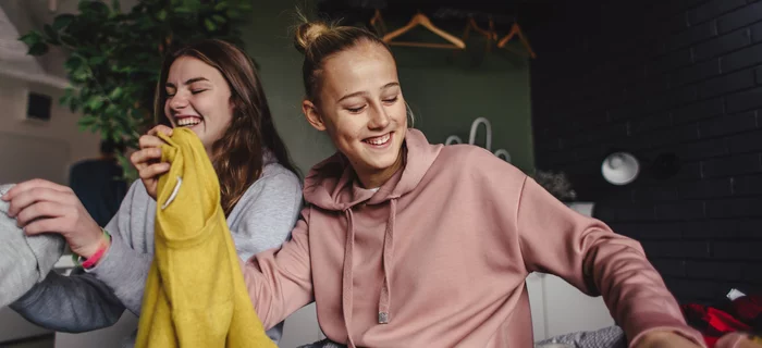 Two young women holding up tops at a clothes swap