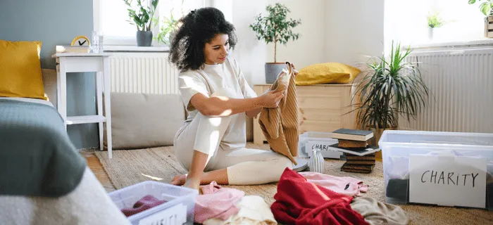 A young woman sitting on the floor putting clothes into boxes for charity