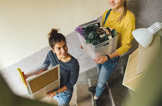 two students walk down stairs carrying boxes