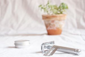 Metal reusable container, razor and a plant in the background