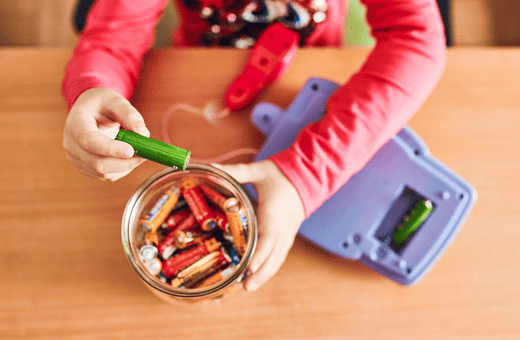 A used battery from a toy is being placed into a jar of other used batteries