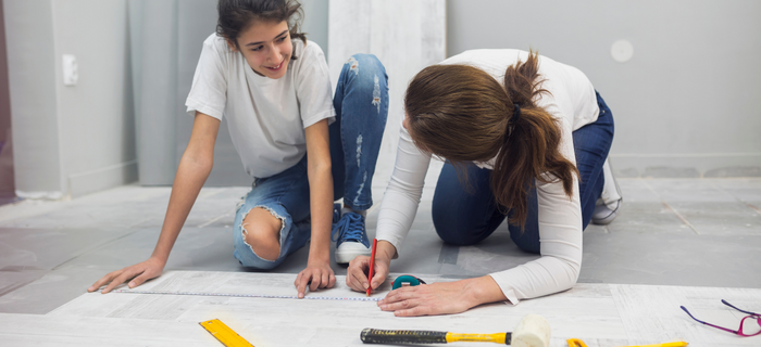 Two women kneeling to mark measurements on laminate flooring