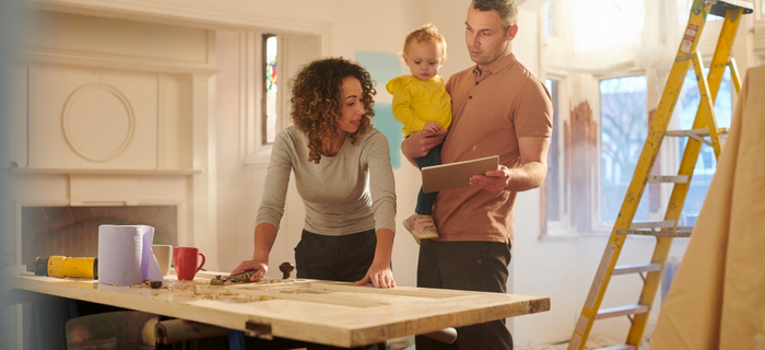 A woman sanding a doorway while her husband holds their child