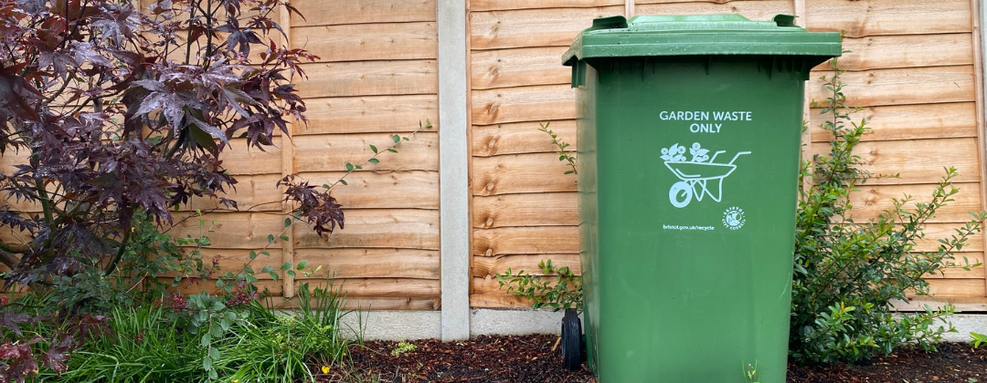 A Bristol garden waste bin in front of a wooden fence
