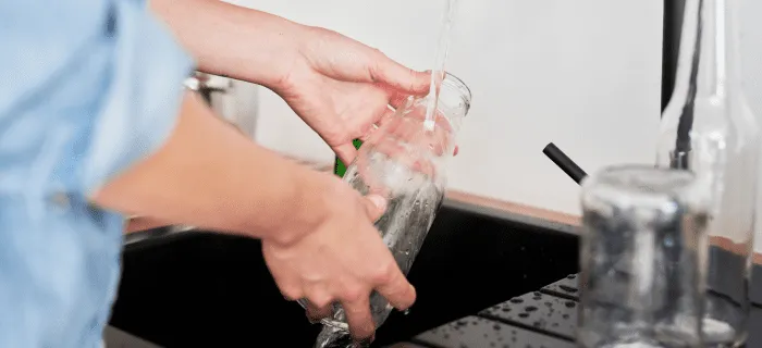 A person is washing a glass milky bottle at a kitchen sink.