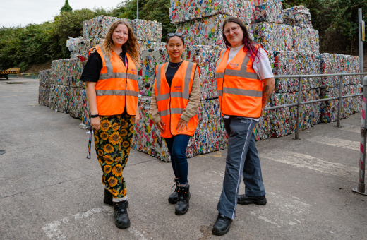A group of three women wearing orange hi vis vests and standing in front of baled metal