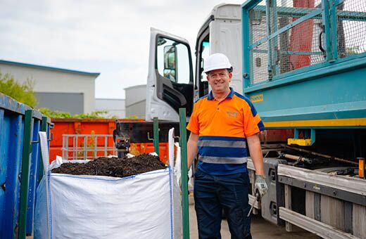 A man with hi-viz and a white hat standing next to a large bag of compost