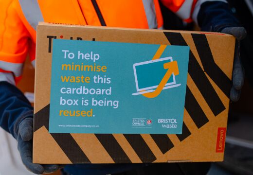 Person carrying back that reads "to help minimise waste this cardboard box is being reused."