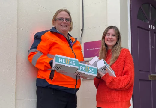 Two women smiling, holding boxes that say "reuse"