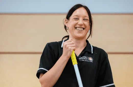 Woman smiling, holding mop handle, with Bristol Waste facilities services clothing