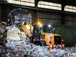 A tractor is scooping plastic recycling up onto a conveyer belt to be recycled