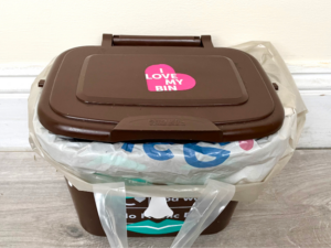 A brown Bristol Waste food recycling caddy sits on a counter top. It's been lined with a Tesco carrier bag