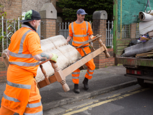 Two Bristol Waste employees in hi-vis carry an old sofa to their truck, ready to take it to be recycled